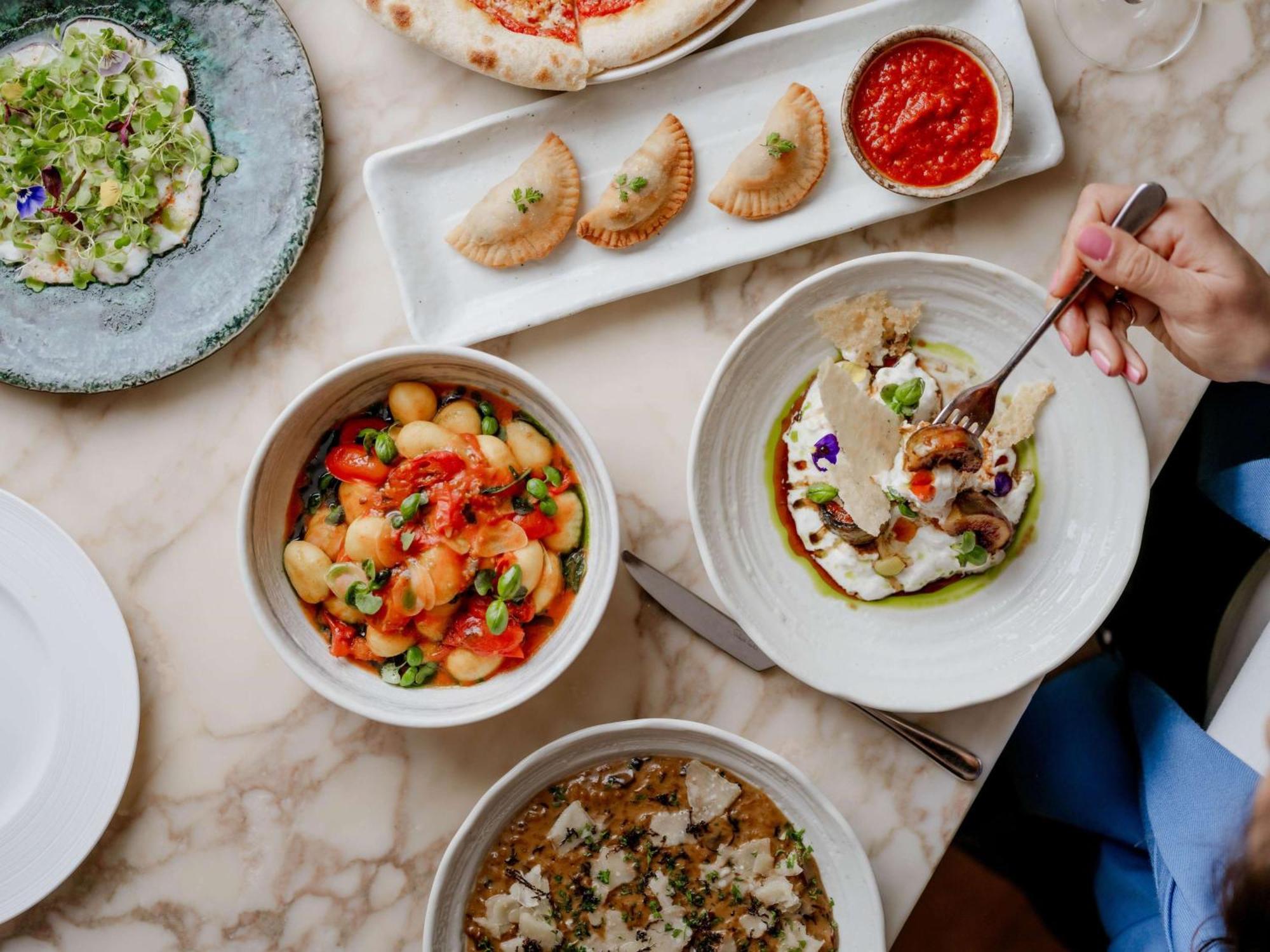 The May Fair, A Radisson Collection Hotel, Mayfair London Luaran gambar The photo showcases a beautifully arranged table filled with various dishes. In the foreground, there are three bowls: one containing a colorful mix of gnocchi with vibrant toppings, another featuring a dish with what appears to be fish or seafood, g